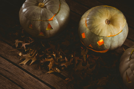 High angle view of illuminated white jack o lanterns with autumn leaves on tableの写真素材