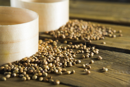 Plastic bowls and coriander seeds scattered on wooden tableの写真素材