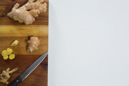 Directly above view of fresh chopped ginger with knife on wooden cutting board over white backgroundの写真素材