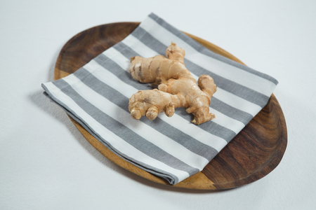 Close up of fresh ginger on striped napkin in wooden plate over white backgroundの写真素材
