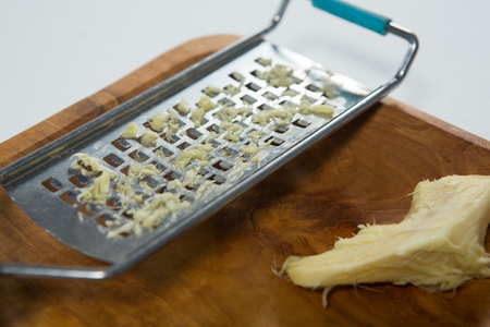 Close up of steel grater and ginger on wooden plate over white backgroundの写真素材