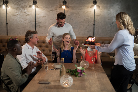 Woman receiving surprise birthday cake from her friends in restaurantの写真素材