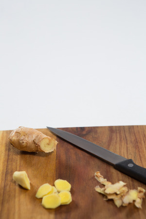 Close up of fresh ginger and knife on wooden cutting board against white backgroundの写真素材