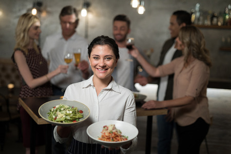 Portrait of smiling waitress holding food in bowl at restaurantの写真素材