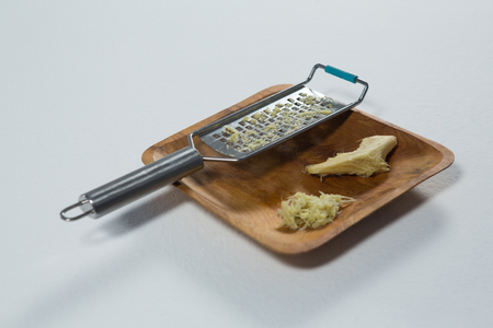 High angle view of steel grater and ginger on wooden plate over white backgroundの写真素材