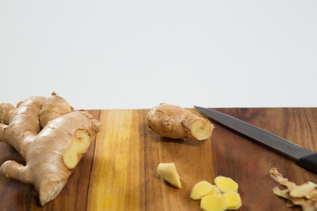 Close up of fresh chopped ginger and knife on wooden cutting board against white backgroundの写真素材