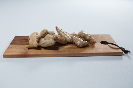 Close up of fresh gingers on wooden serving board against white background