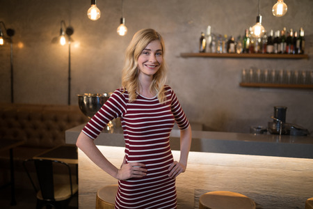 Portrait of beautiful woman standing with hands on hip at counter in resturantの写真素材