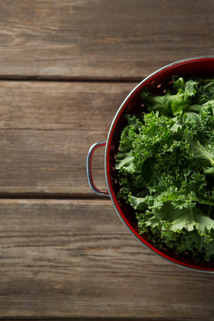 Overhead view of fresh kale in colander on wooden tableの写真素材