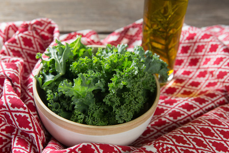High angle view of fresh kale leaves in bowl with oil bottle and fabric on tableの写真素材
