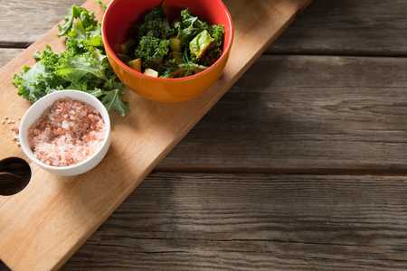 High angle view of fresh kale with rock salt on cutting board at tableの写真素材