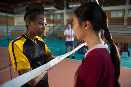 Female players standing with arms crossed and staring each other in the volleyball courtの写真素材