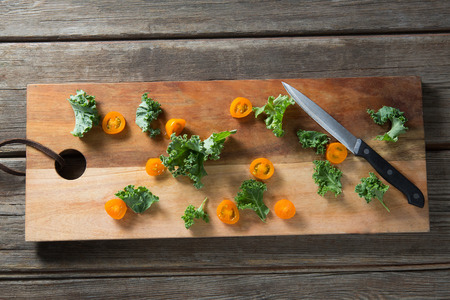 Overhead view of fresh kale vegetable with tomato slices on cutting board with knife at wooden tableの写真素材