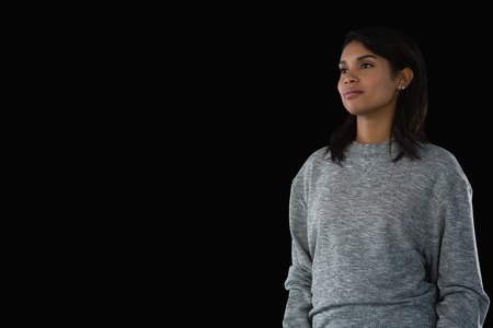 Smiling young woman looking away while standing against black backgroundの写真素材