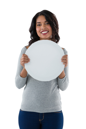 Portrait of smiling young woman holding circle shaped placard against white backgroundの写真素材