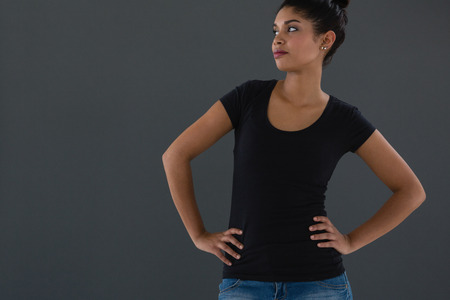 Young woman with hands on hip standing against gray backgroundの写真素材