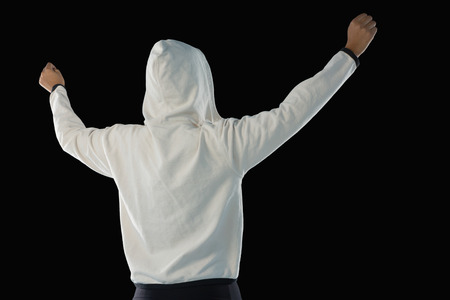 Rear view of female athlete in hooded jacket standing with arms raised against black backgroundの写真素材