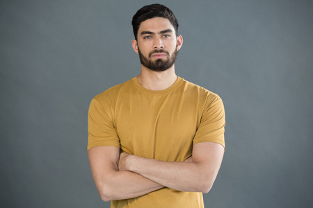 Portrait of handsome man posing with arms crossed against grey backgroundの写真素材