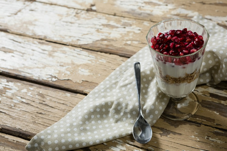 Cup of yogurt muesli and pomegranate with napkin and spoon on tableの写真素材