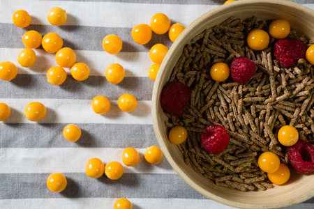 Bowl of cereal bran stick with golden berries and raspberries on table