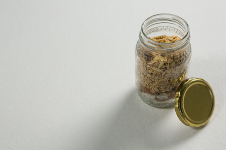Homemade granola or muesli in open glass jar on white background