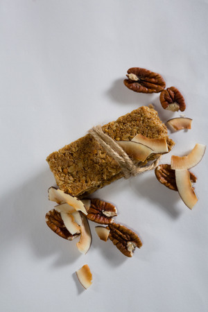 Granola bar tied with string and dried fruits kept around on white backgroundの写真素材