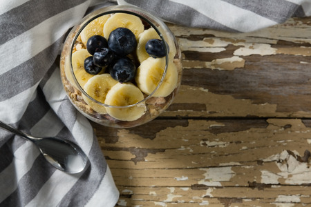 Cup of yogurt muesli, banana and blueberries for breakfast on wooden tableの写真素材
