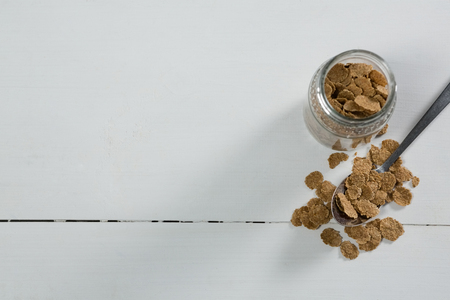 Wheat flakes in glass jar and spoon on tableの写真素材