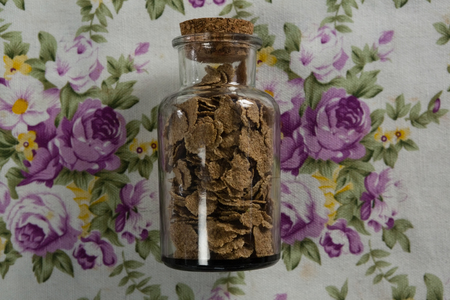 Wheat flakes in glass jar on floral backgroundの写真素材