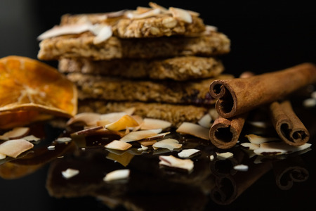 Granola bars with dried coconut, cinnamon sticks and orange slices on black background