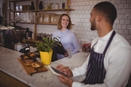 Smiling young waiter and waitress standing at counter in coffee shopの写真素材