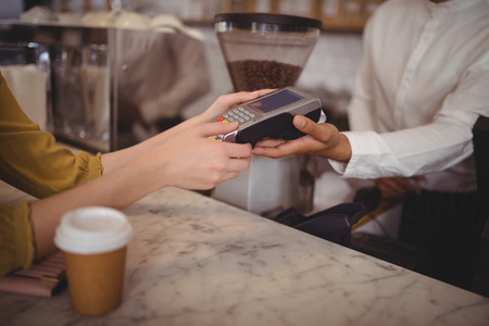 High angle view of female customer paying through debit card at counter in coffee shopの写真素材