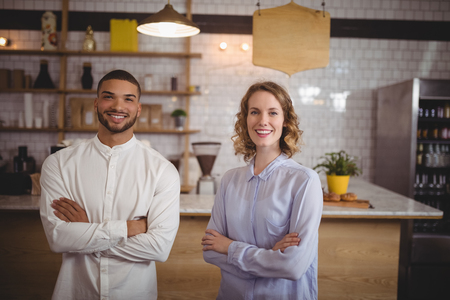 Portrait of smiling young friends standing with arms crossed at coffee shopの写真素材