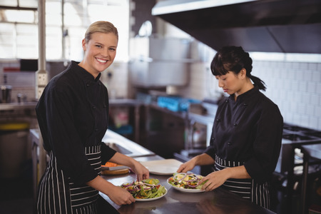 Portrait of smiling female chefs preparing fresh Greek salad at kitchen counter in cafe
