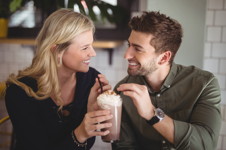 Smiling young couple holding fresh dessert in glass at coffee shopの写真素材