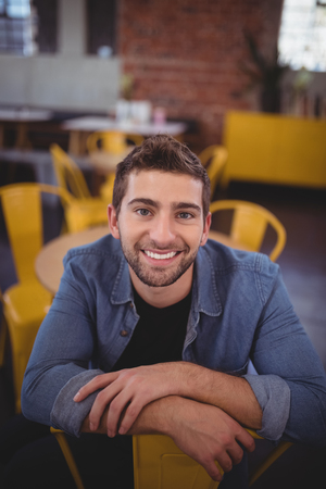 Portrait of smiling handsome man sitting on chair at coffee shopの写真素材