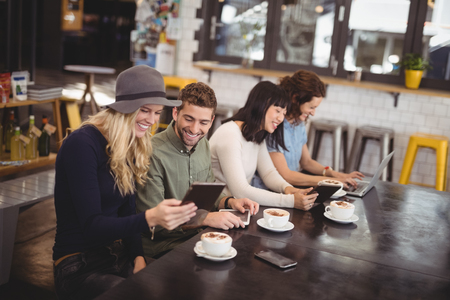 High angle view of happy friends using technologies while sitting at table in coffee shopの写真素材