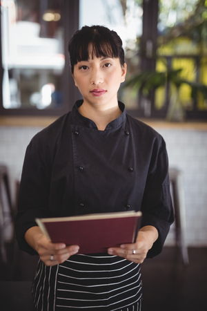 Portrait of confident young waitress holding menu at coffee shopの写真素材