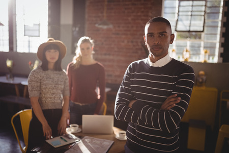 Portrait of confident man standing against female colleagues at coffee shopの写真素材
