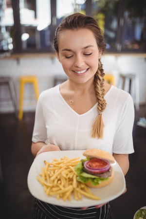 Smiling young waitress holding fresh junk food plate at cafeの写真素材