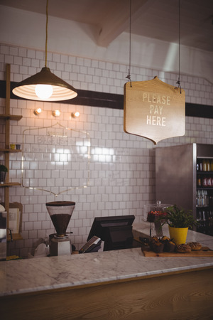 Text and pendant light hanging over counter against white wall at cafeの写真素材