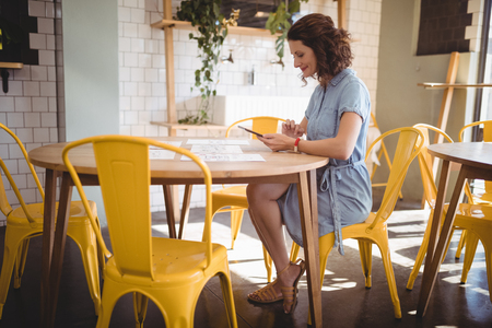 Side view of young woman sitting tablet and papers at table in coffee shopの写真素材