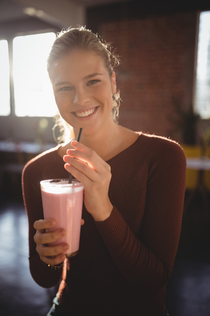Portrait of smiling young woman sitting with milkshake at cafeの写真素材