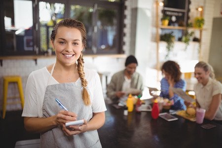 Portrait of smiling young waitress with notepad standing at cafeの写真素材