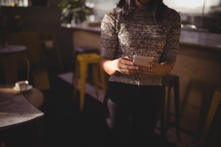 Midsection of female customer using mobile phone while standing at coffee shopの写真素材