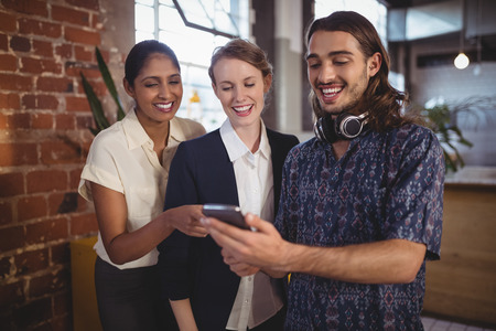 Young man showing smartphone to female friends while standing at coffee shop