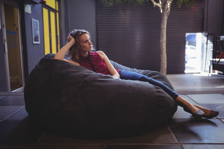 Young female customer relaxing on bean bag against wallの写真素材
