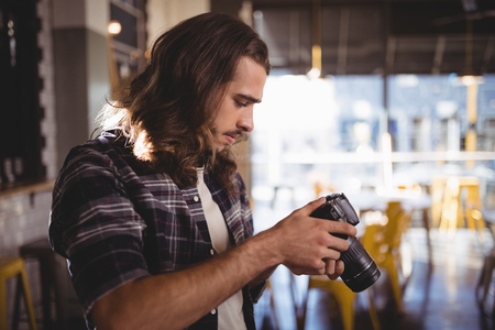 Side view of young male photographer holding DSLR camera at coffee shopの写真素材