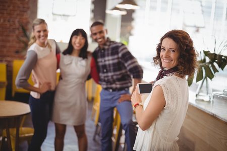 Portrait of smiling woman photographing young friends from smartphone at coffee shopの写真素材