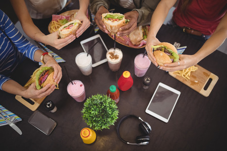 High angle view of friends holding fresh food at table in coffee shopの写真素材